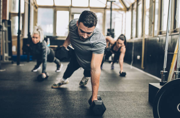 two young fitness women exercise with dumbbell with personal trainer in the gym